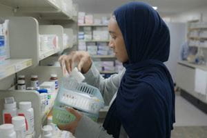 A pharmacist sorts medications at a pharmacy shelf